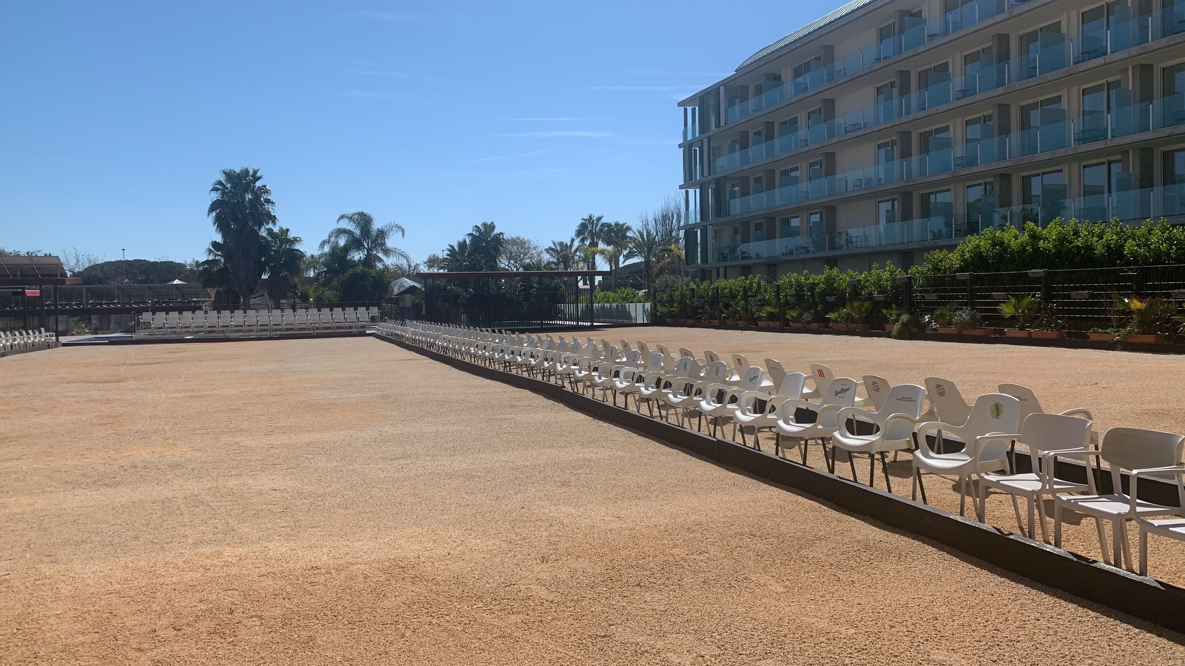 An outdoor seating area with rows of white plastic chairs and a gravel surface.