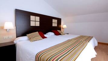 A hotel room with a large bed, two bedside lamps, a dark headboard, and a striped throw blanket.