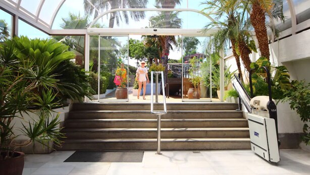 Un invernadero con entrada de cristal, palmeras y plantas en macetas.