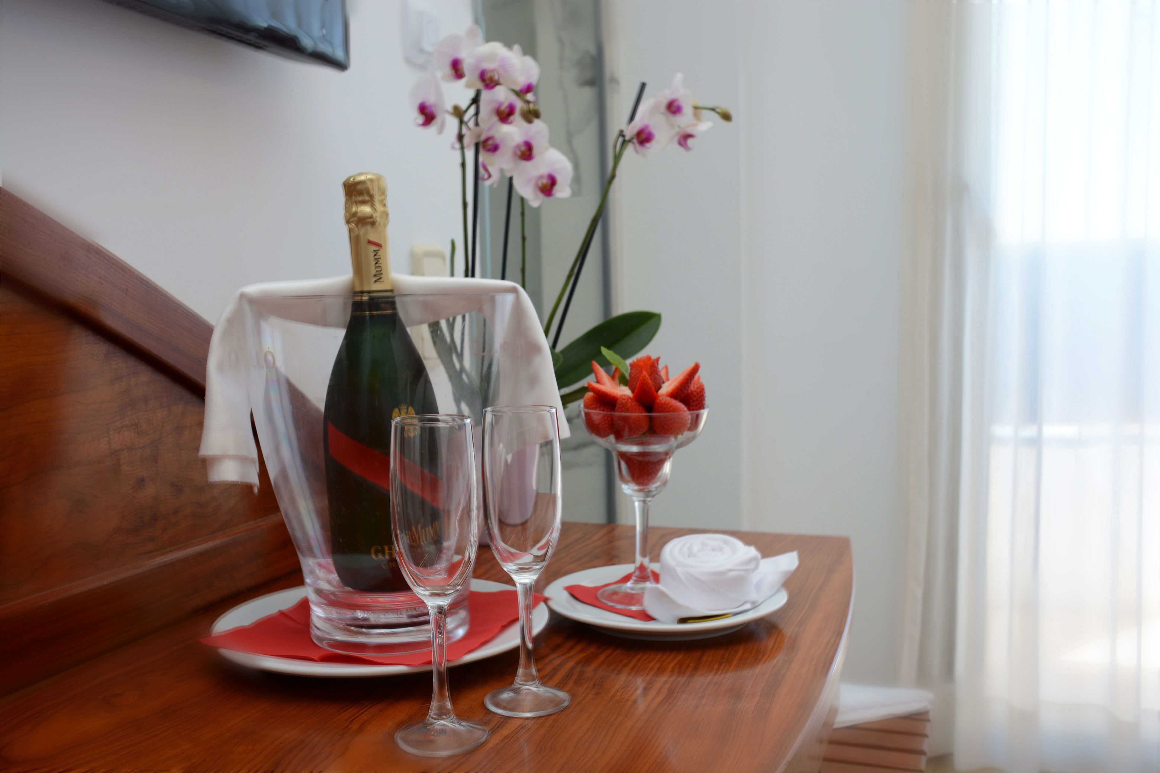 A table with a bottle of champagne, two glasses, a plate with strawberries, and a vase with orchids.