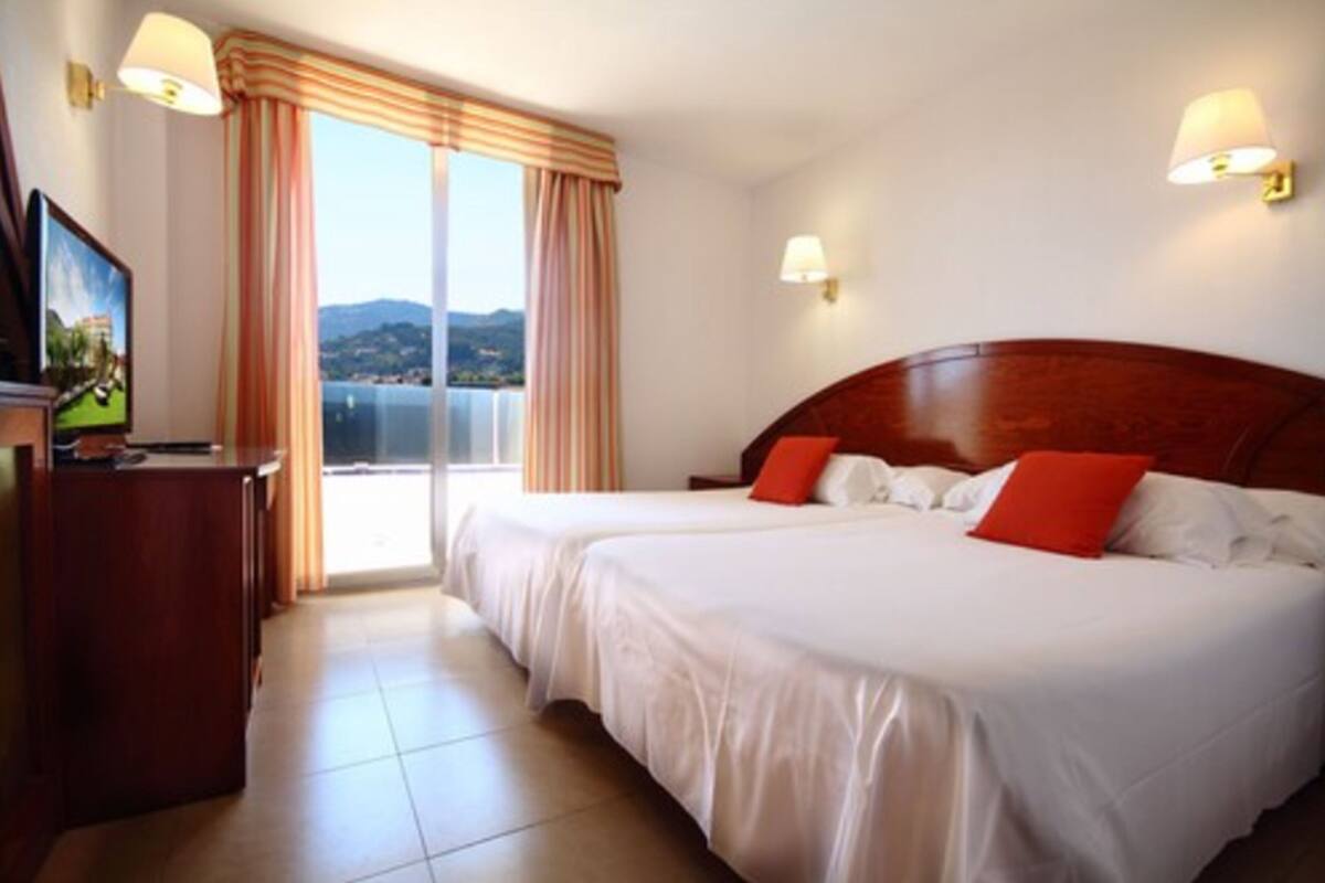 A hotel room with two beds, a TV, and a view of the sea.