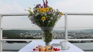 A table with a floral arrangement, pastries, and a cup on a balcony with a city view. - Centre Hotel (Kaunas)