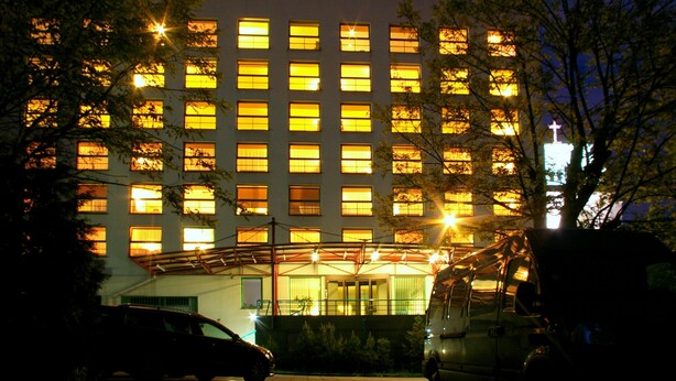 A multi-story building with numerous windows, a gated entrance, and a parking area with vehicles. - Centre Hotel (Kaunas)