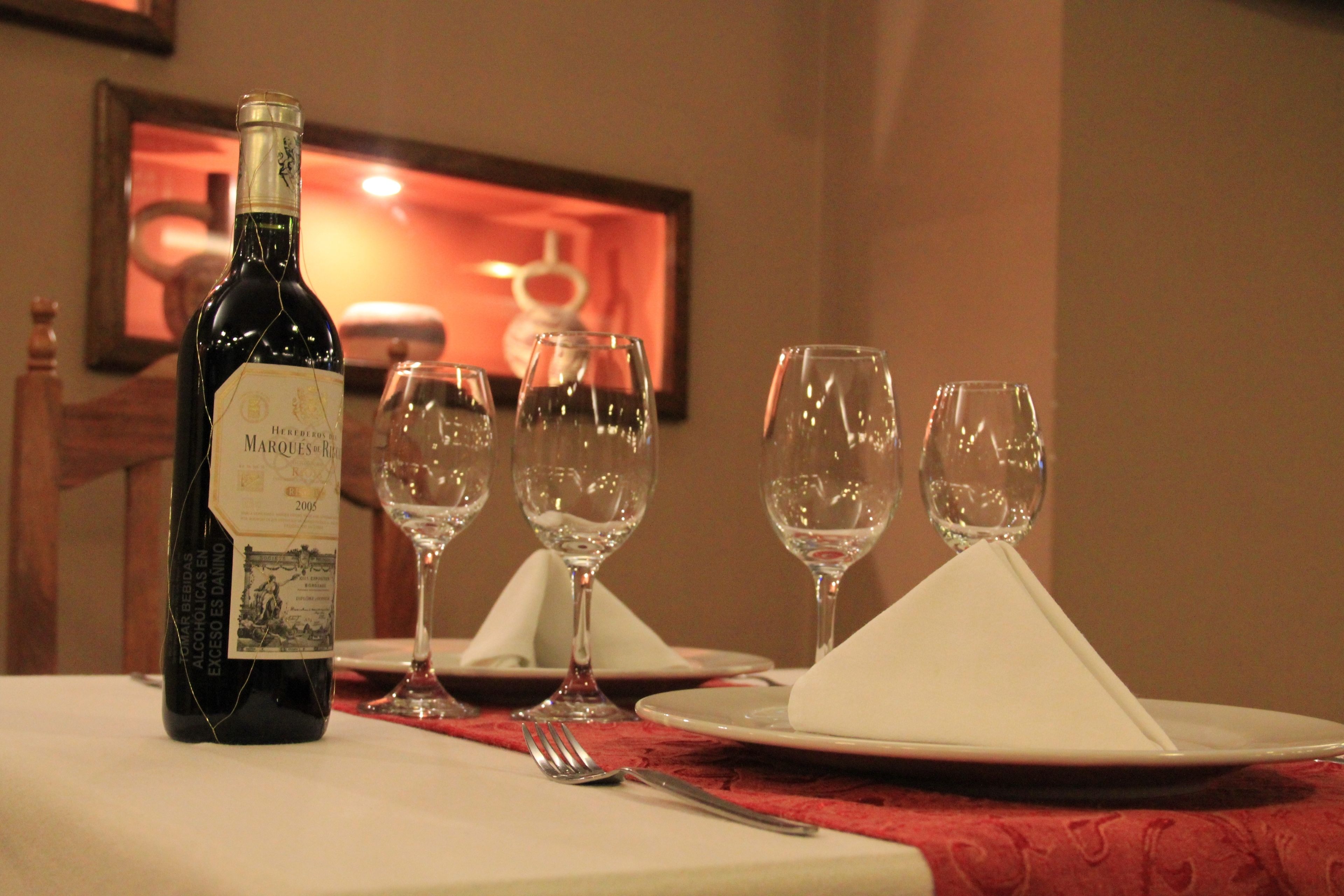 Una mesa servida con una botella de vino, copas y platos, lo que sugiere una preparación para comer.