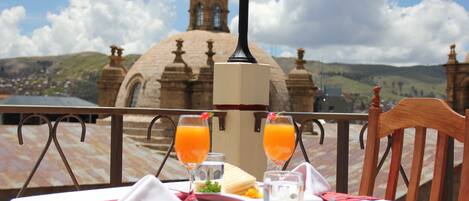 Una mesa servida con comida y dos vasos de jugo de naranja, con vista a un edificio histórico con cúpulas y una cruz en la parte superior.