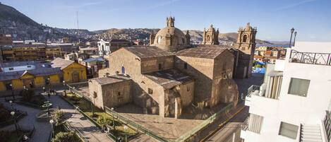 A historic building with a prominent dome and bell towers, surrounded by urban buildings and a hilly landscape.