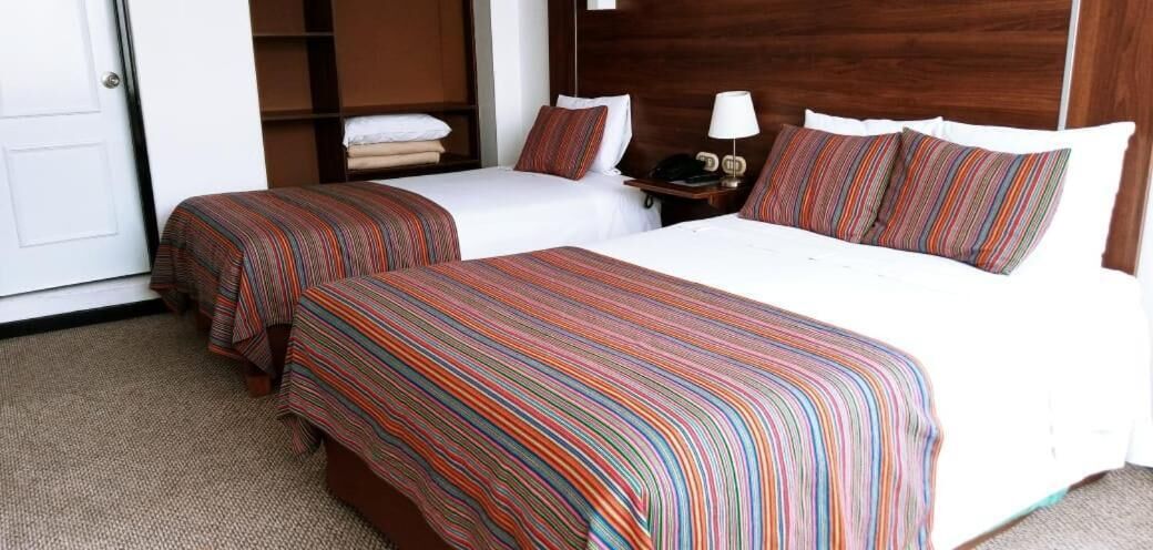 A hotel room with two single beds, a large bed, a nightstand with a lamp, and a wardrobe.