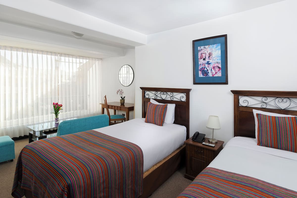 Une chambre d’hôtel avec deux lits, un bureau, une chaise et une fenêtre avec des rideaux.