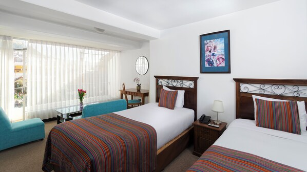 Habitación de hotel con dos camas, un escritorio, una silla y un ventanal con cortinas.