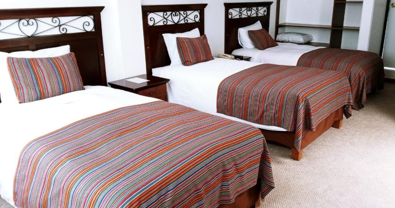 Habitación de hotel con tres camas, cada una con cubrecama a rayas, cabeceros de madera y ropa de cama blanca.