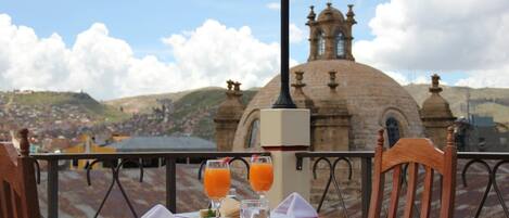 A table set with a white tablecloth, two glasses of orange juice, and a small plate with food. A lamp post is visible in the foreground.