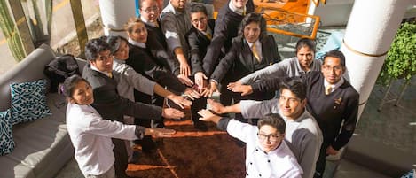 A group of people in business attire gathered in a circle on a carpeted area with a staircase in the background.