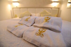 Un letto rifatto con lenzuola bianche e asciugamani ricamati in oro.
