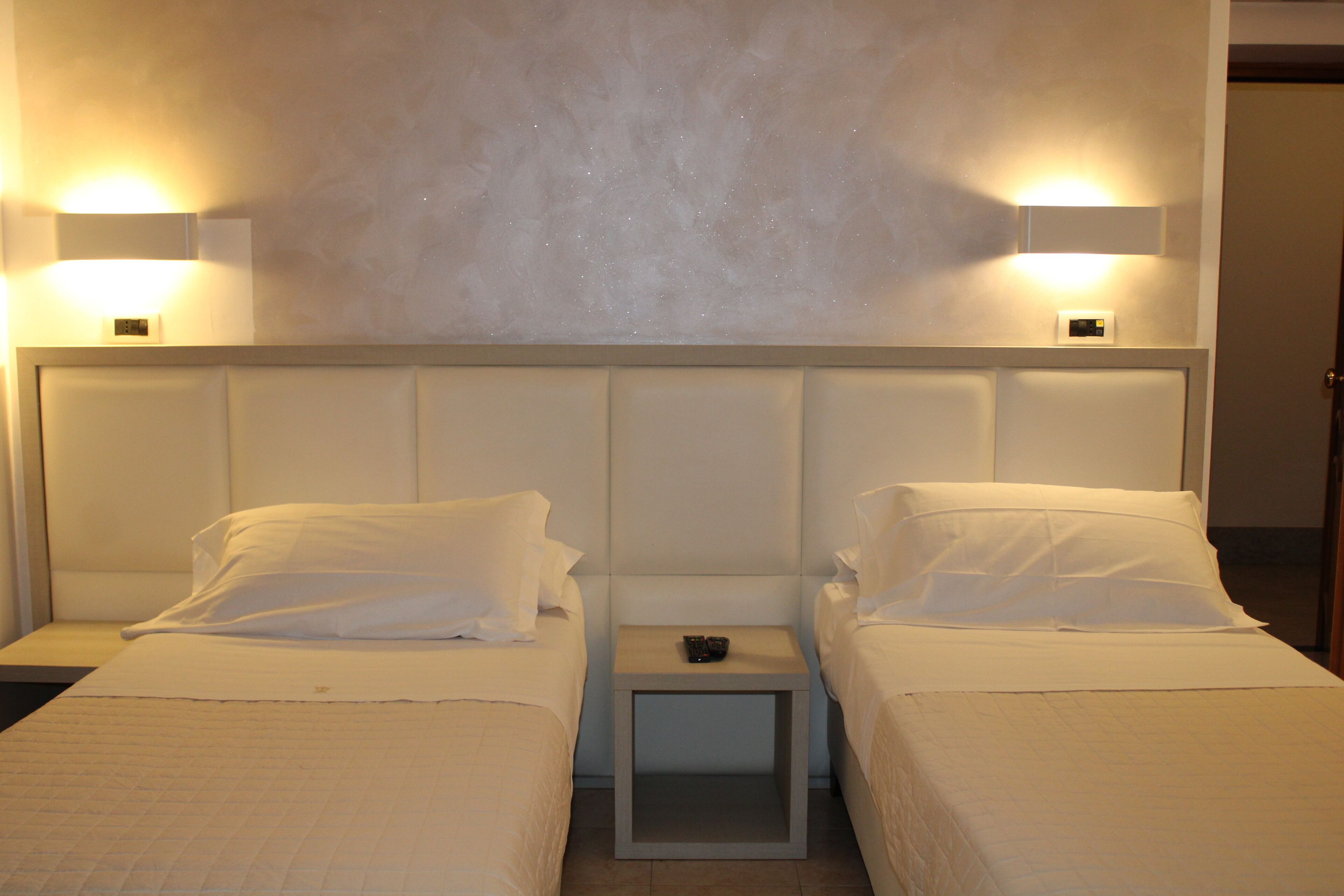 Una camera d'albergo con due letti, un comodino e luci a parete.