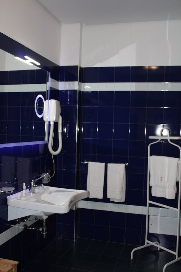 Un baño con lavamanos blanco, un espejo, un secador de pelo y dos toallas blancas en un perchero.