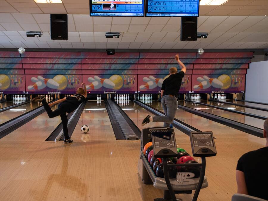 Bolera con varias pistas, una bola de bolos en movimiento y una persona jugando.