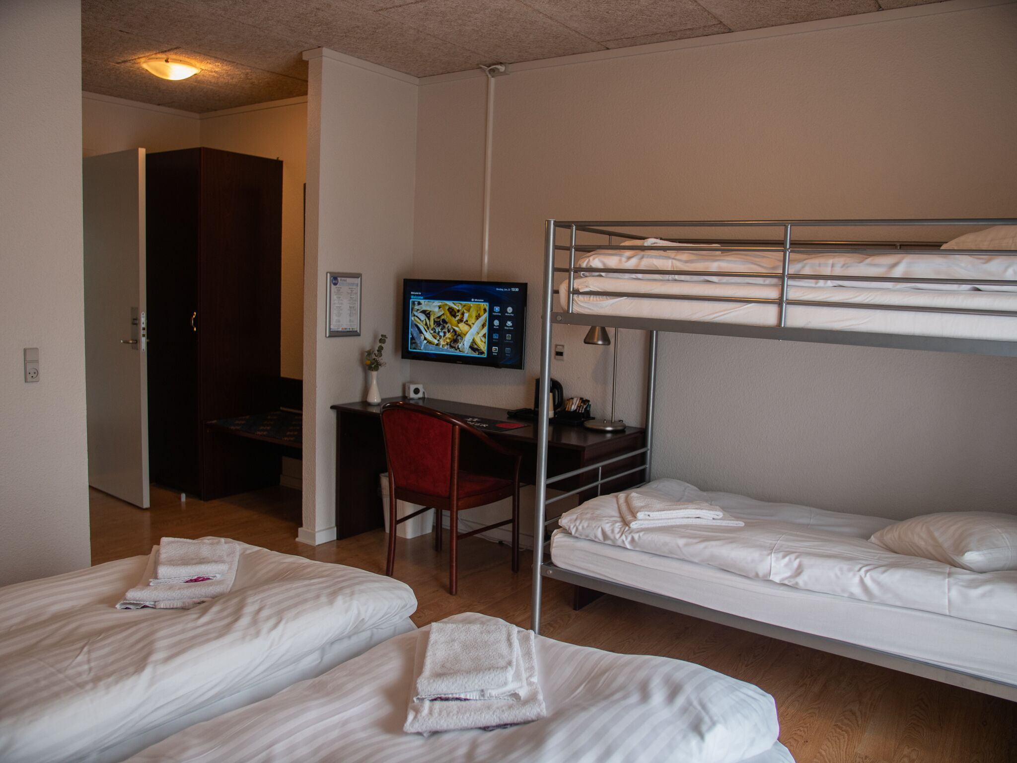 A hotel room with bunk beds, a desk with a computer, a chair, and a TV on the wall.
