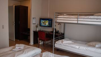 A hotel room with bunk beds, a desk with a computer, a chair, and a TV on the wall.