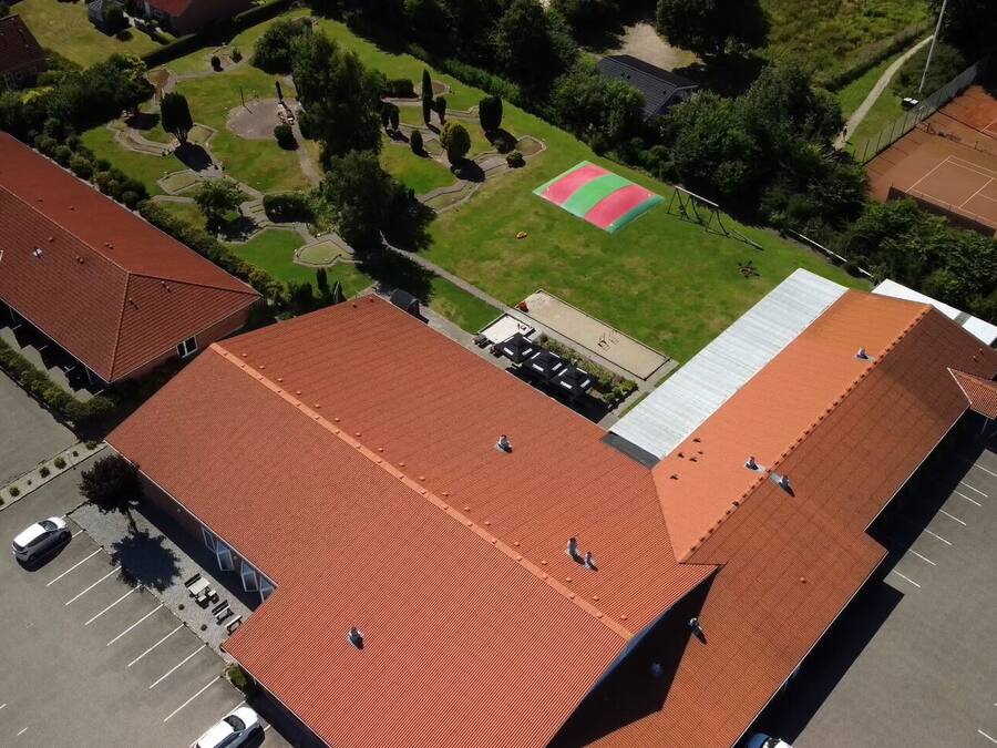 Vista aérea de un edificio con tejado de tejas rojas, cancha de tenis y aparcamiento.