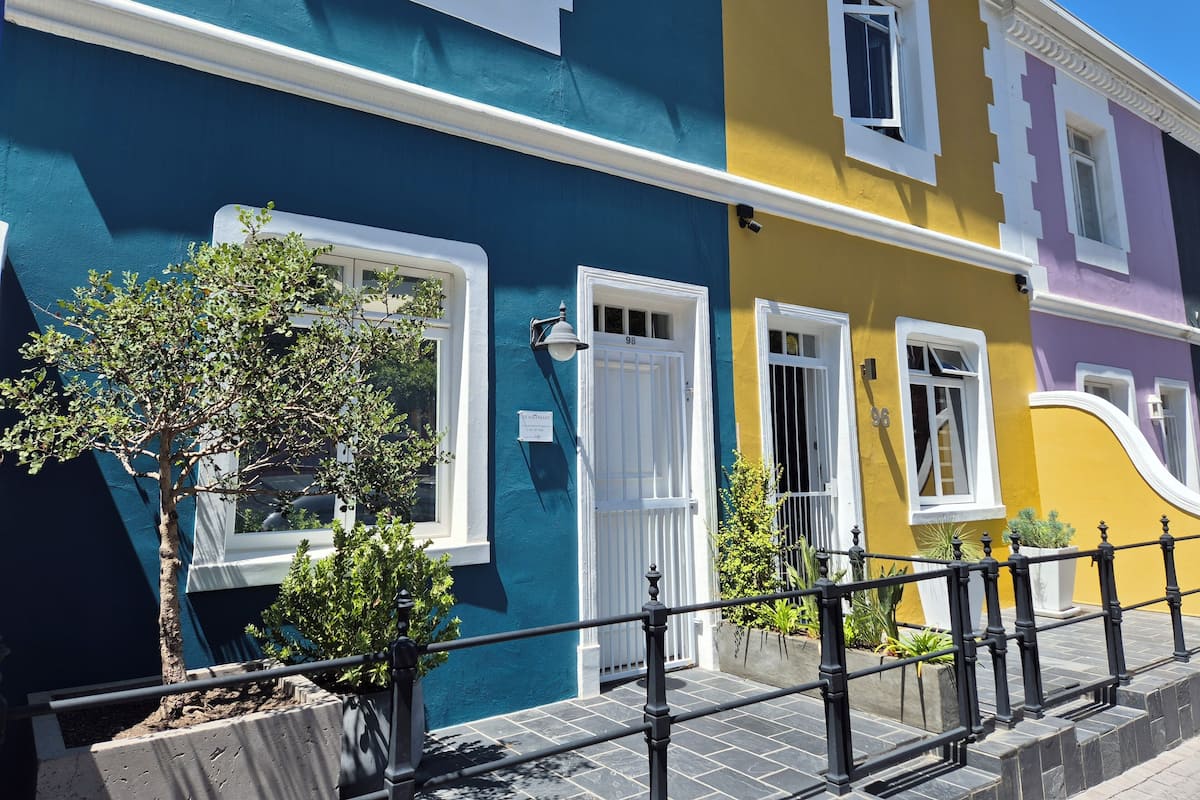 A row of colorful houses with white-framed windows and doors, a small tree, and a black metal railing.