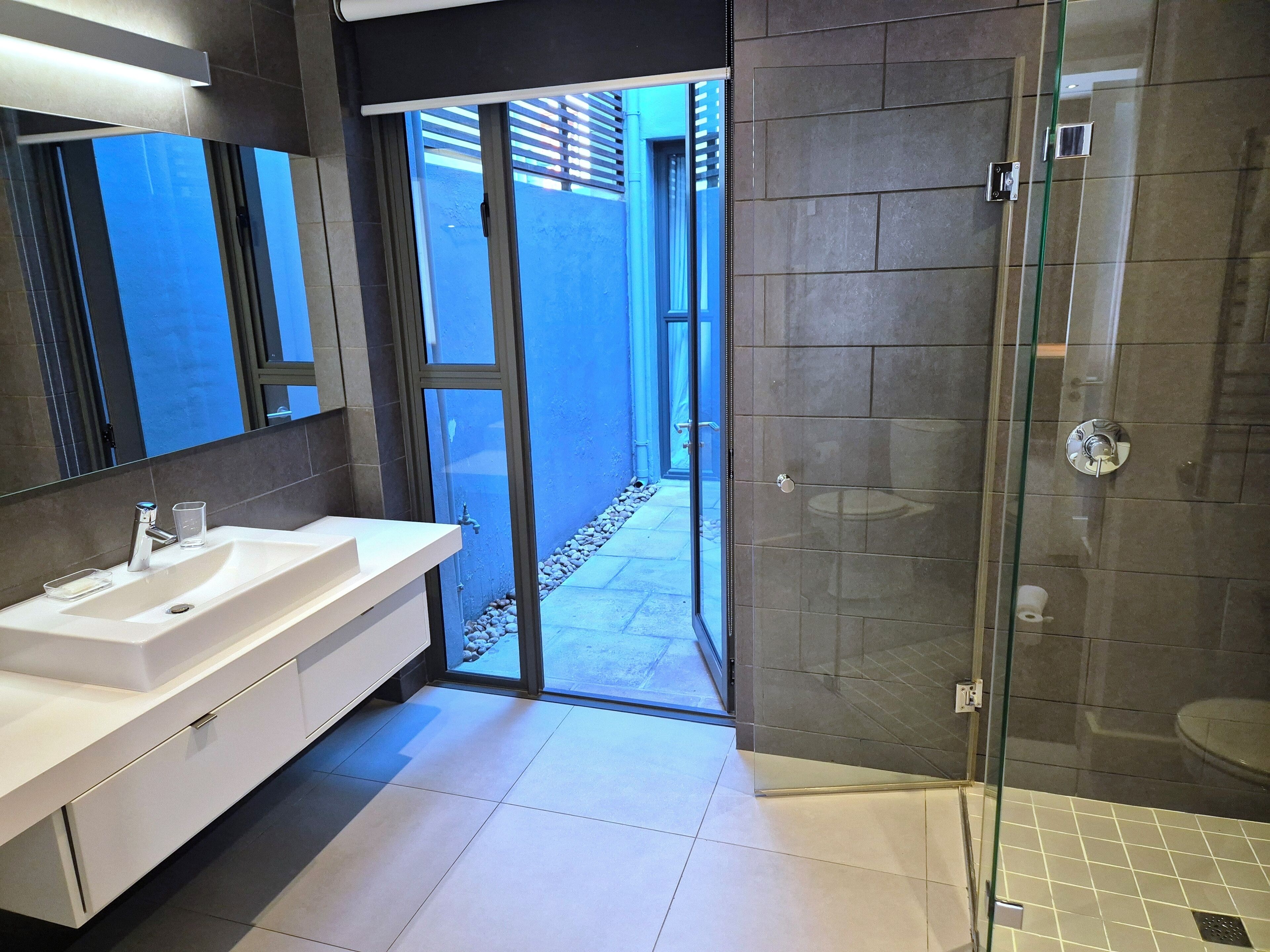 A modern bathroom with a glass shower enclosure, a white sink with a mirror, and a tiled floor.