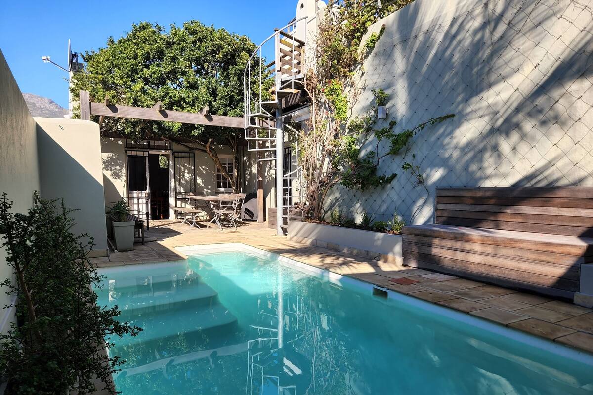 A swimming pool with a wooden deck, a covered outdoor seating area, and a view of a mountainous landscape.