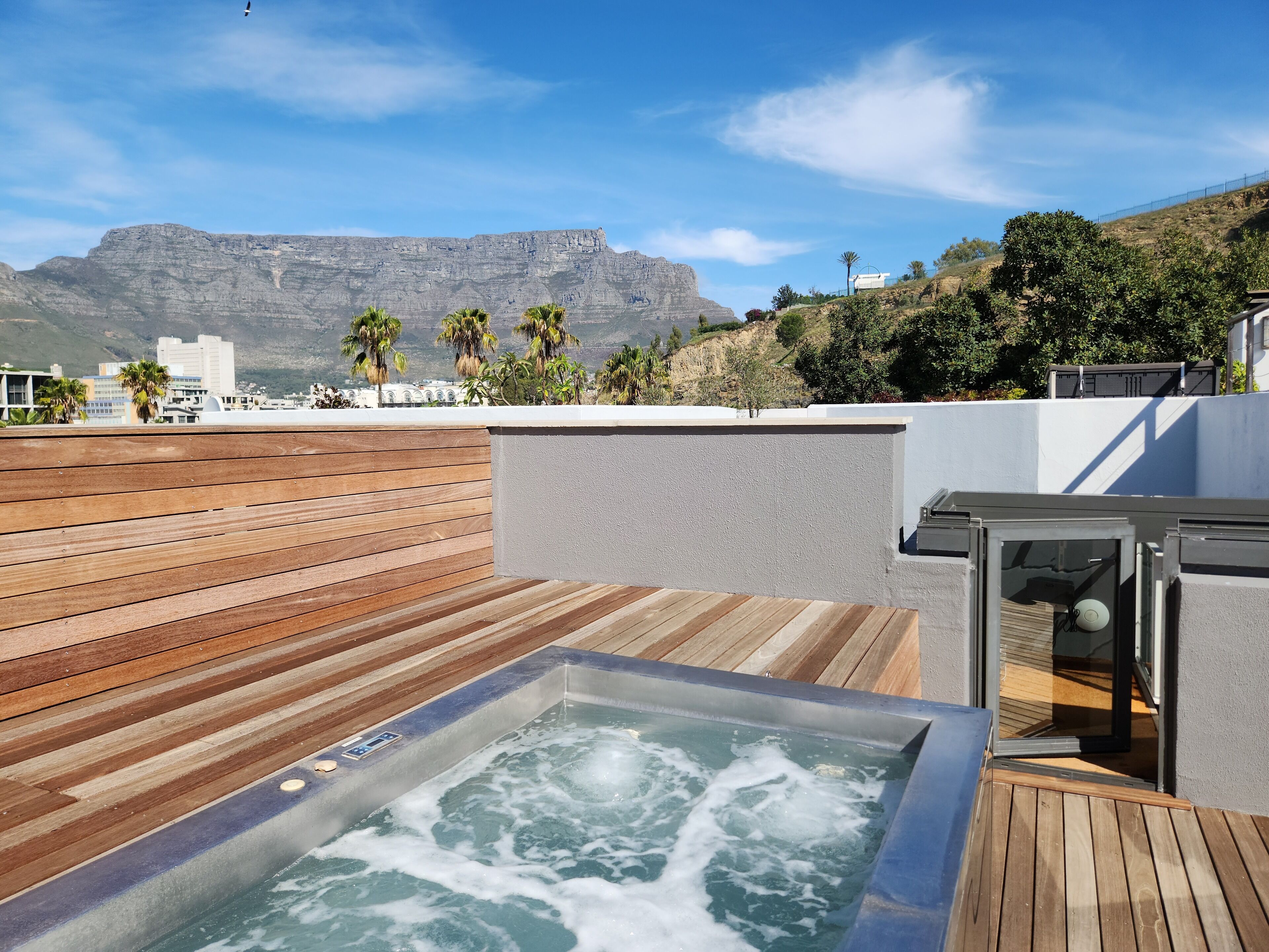 A rooftop terrace with a hot tub, wooden deck, and a view of mountains and buildings.