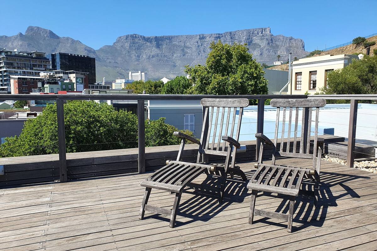 A wooden deck with two wooden chairs and a view of a mountain range in the background.