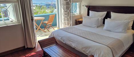 Un dormitorio con una cama grande, un banco de madera, un tapete rojo estampado y vistas a un balcón con una silla.
