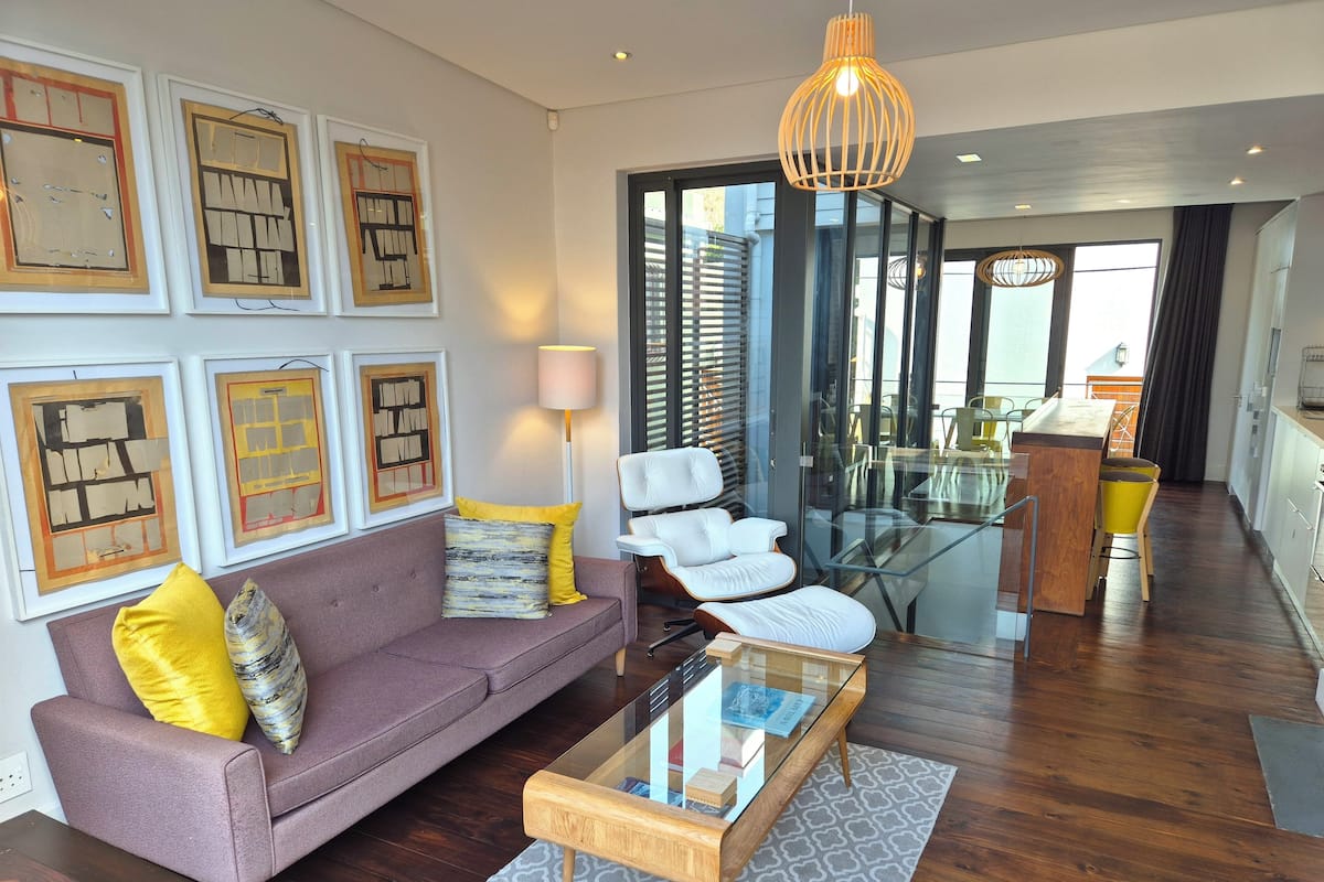 A modern living room with a purple sofa, a glass coffee table, and framed artwork on the wall.