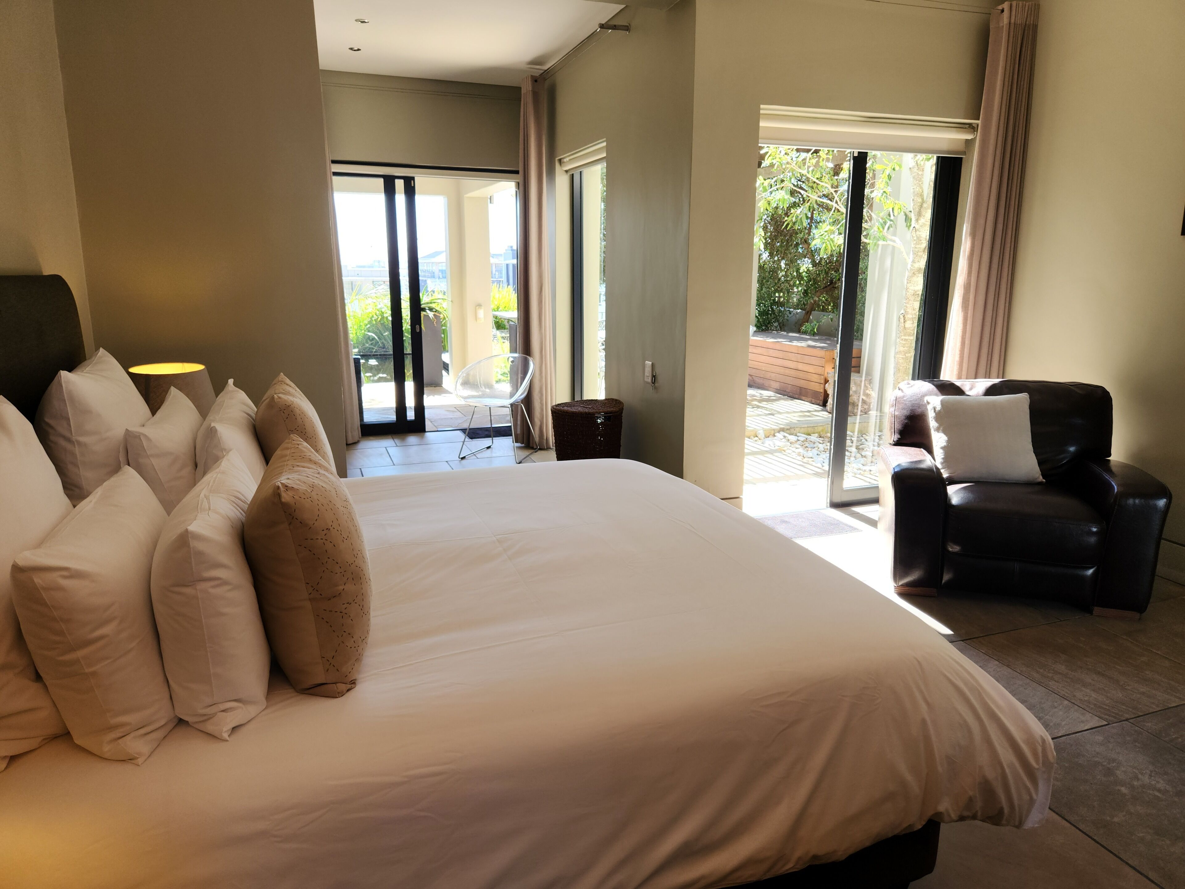 Ein geräumiges Schlafzimmer mit einem großen Bett, einem Sessel und Blick ins Freie durch eine Glastür.