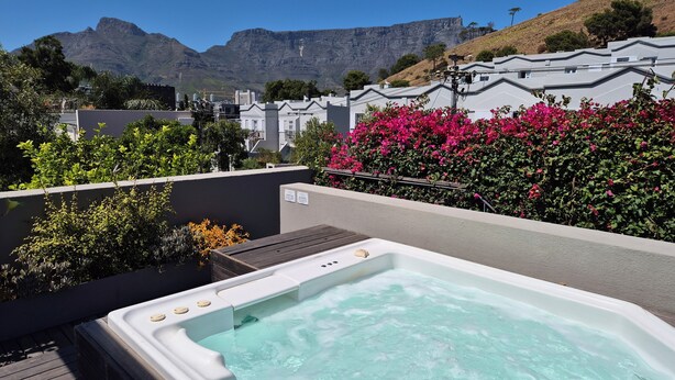 A hot tub on a rooftop with a view of mountains and a row of houses in the background.