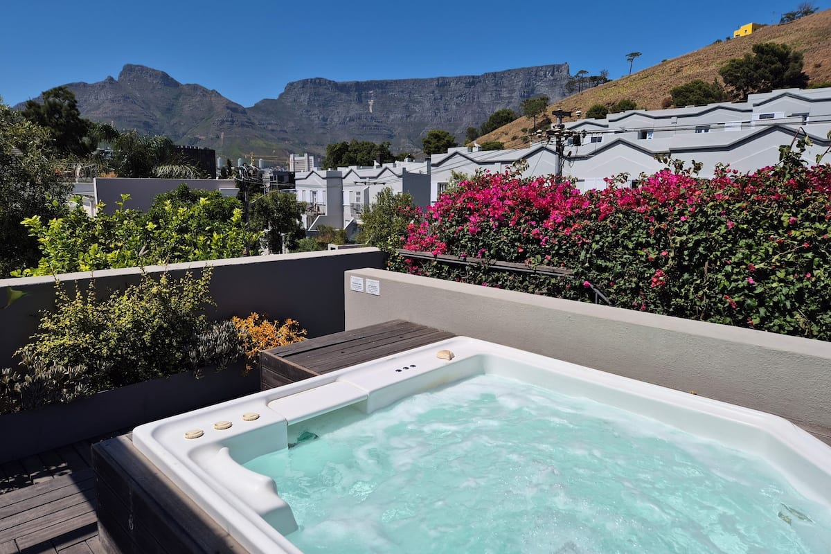 A hot tub on a rooftop with a view of mountains and a row of houses in the background.