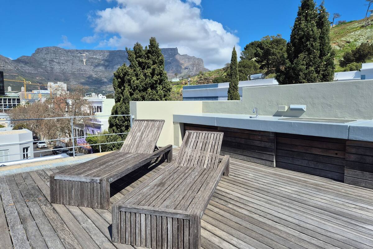 A rooftop terrace with wooden deck seating and a view of a mountain range.