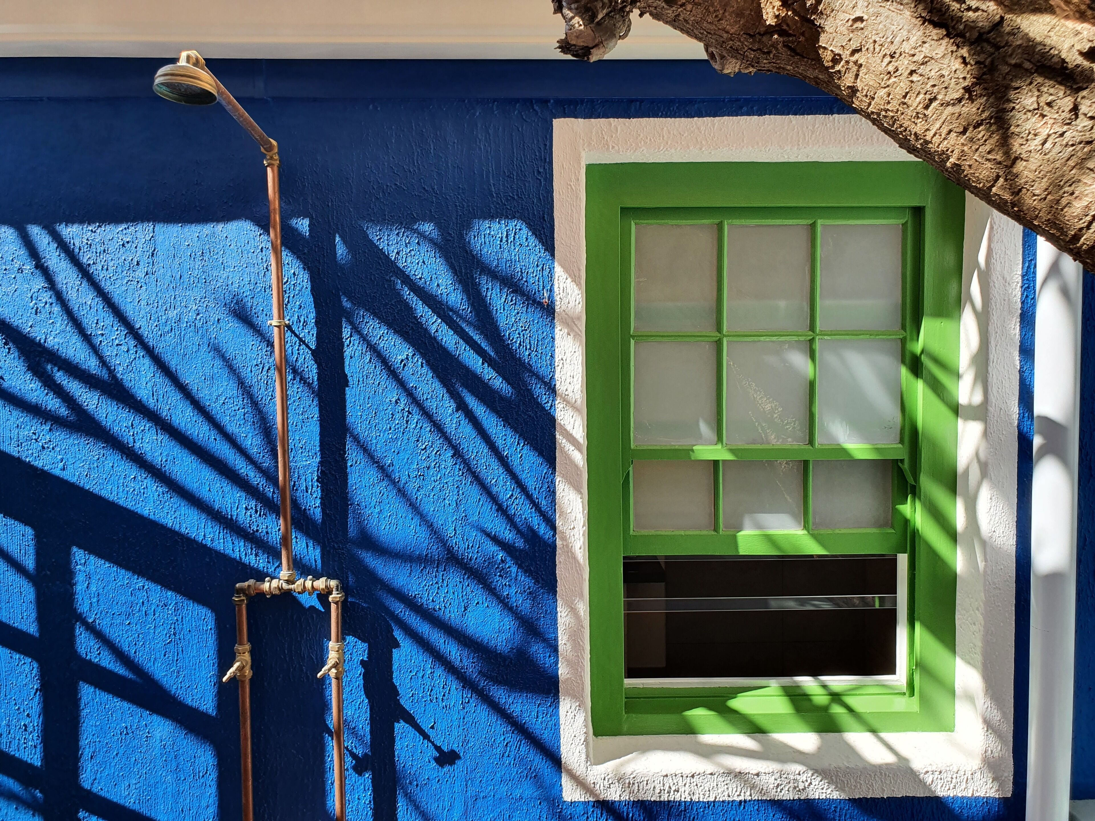 A blue wall with a green window and a brass outdoor light fixture.