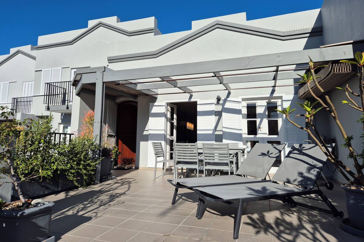 A modern building with a white facade, a balcony with metal railings, and a tiled patio area with outdoor furniture.