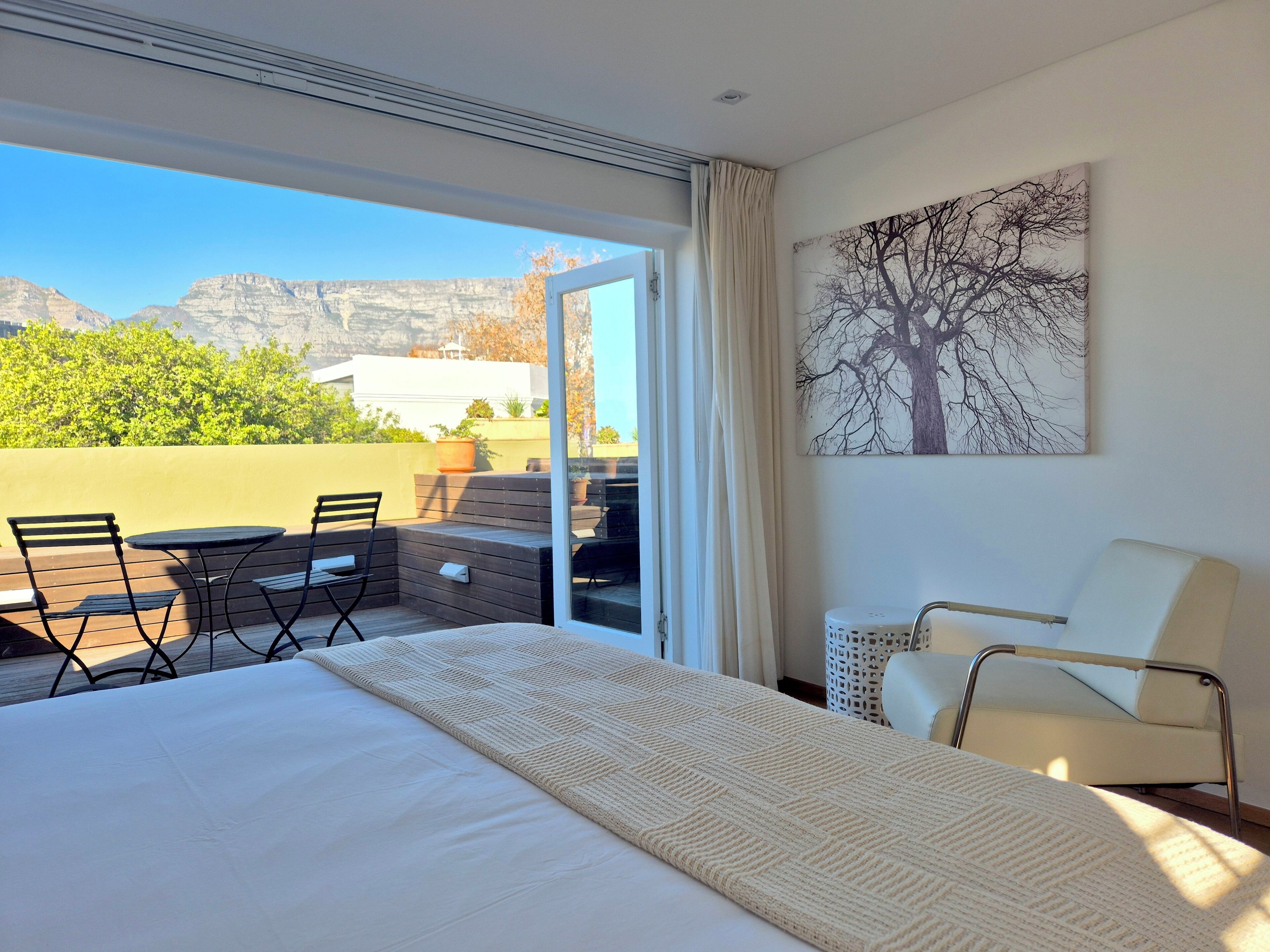 Une chambre d’hôtel avec un lit, une chaise, une table et une vue sur les montagnes, visible à travers une porte vitrée.