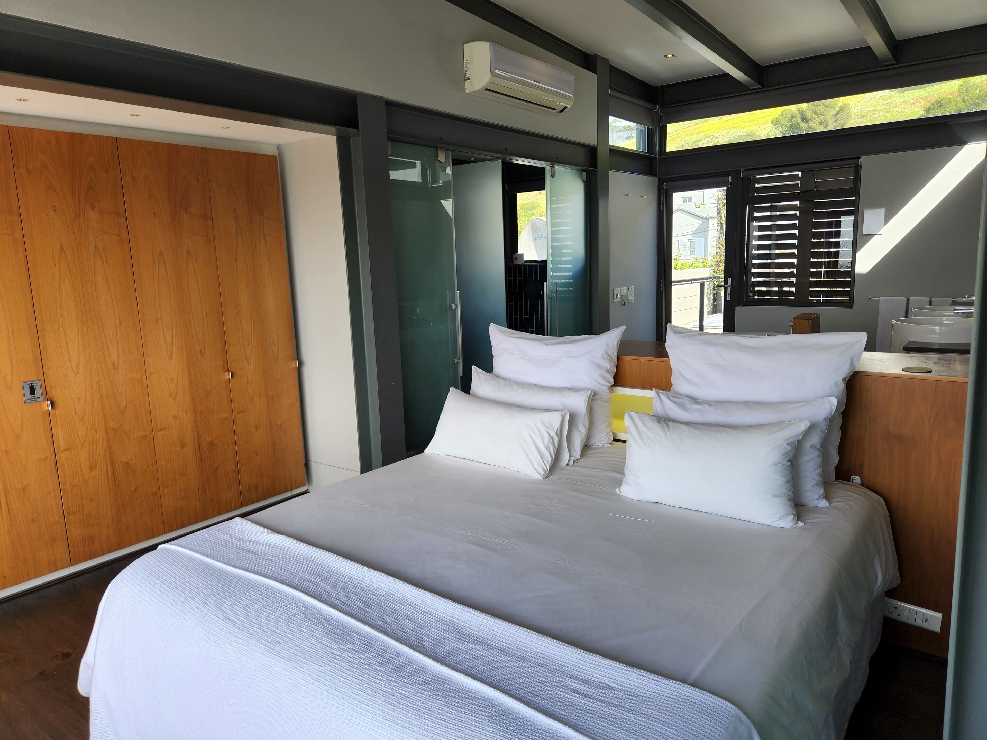 A modern bedroom with a large bed, wooden wardrobe, and a view of the outdoors.