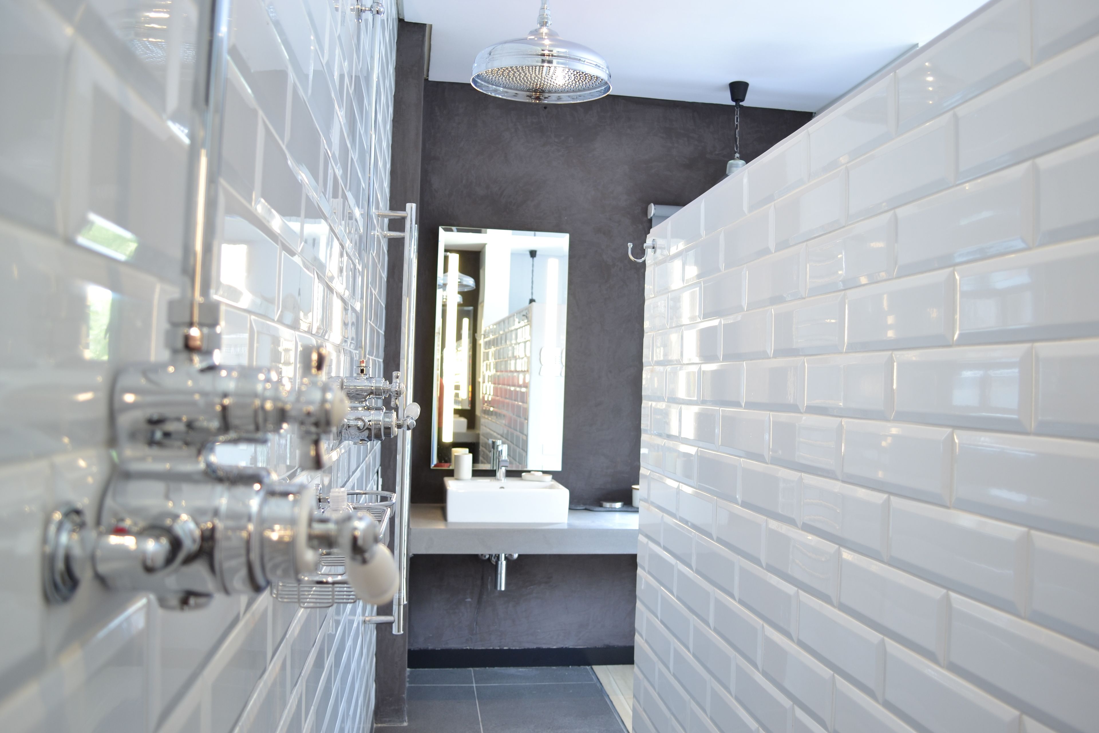 A modern bathroom with white tiled walls, a large mirror, and chrome fixtures.