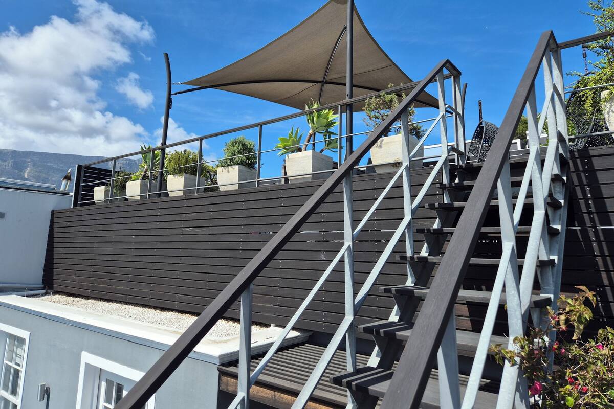 A staircase leading to a rooftop terrace with a large canopy, potted plants, and a view of the sky and distant landscape.