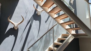 A staircase with wooden steps and glass railings, leading to a room with a large bull skull mounted on the wall.