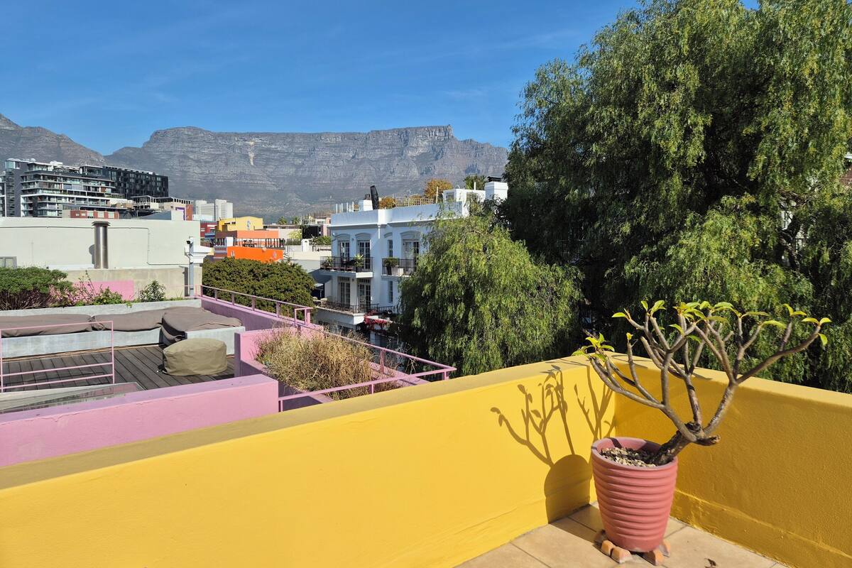 A yellow balcony with a potted plant, overlooking a cityscape with buildings and a mountain in the background.