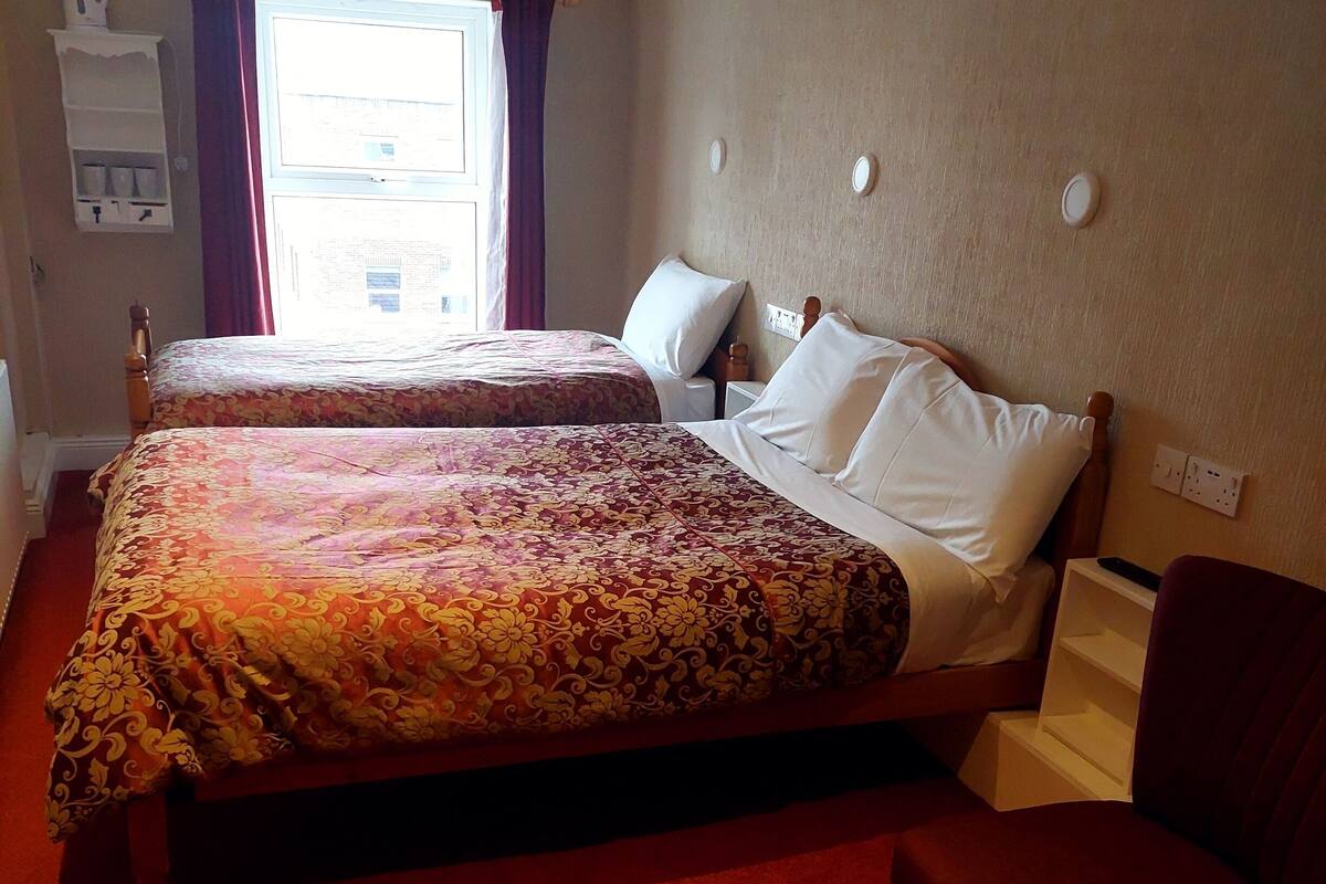 Ein Hotelzimmer mit zwei Betten, einem roten Teppich, einem hölzernen Kopfteil und einem Fenster mit Vorhängen.