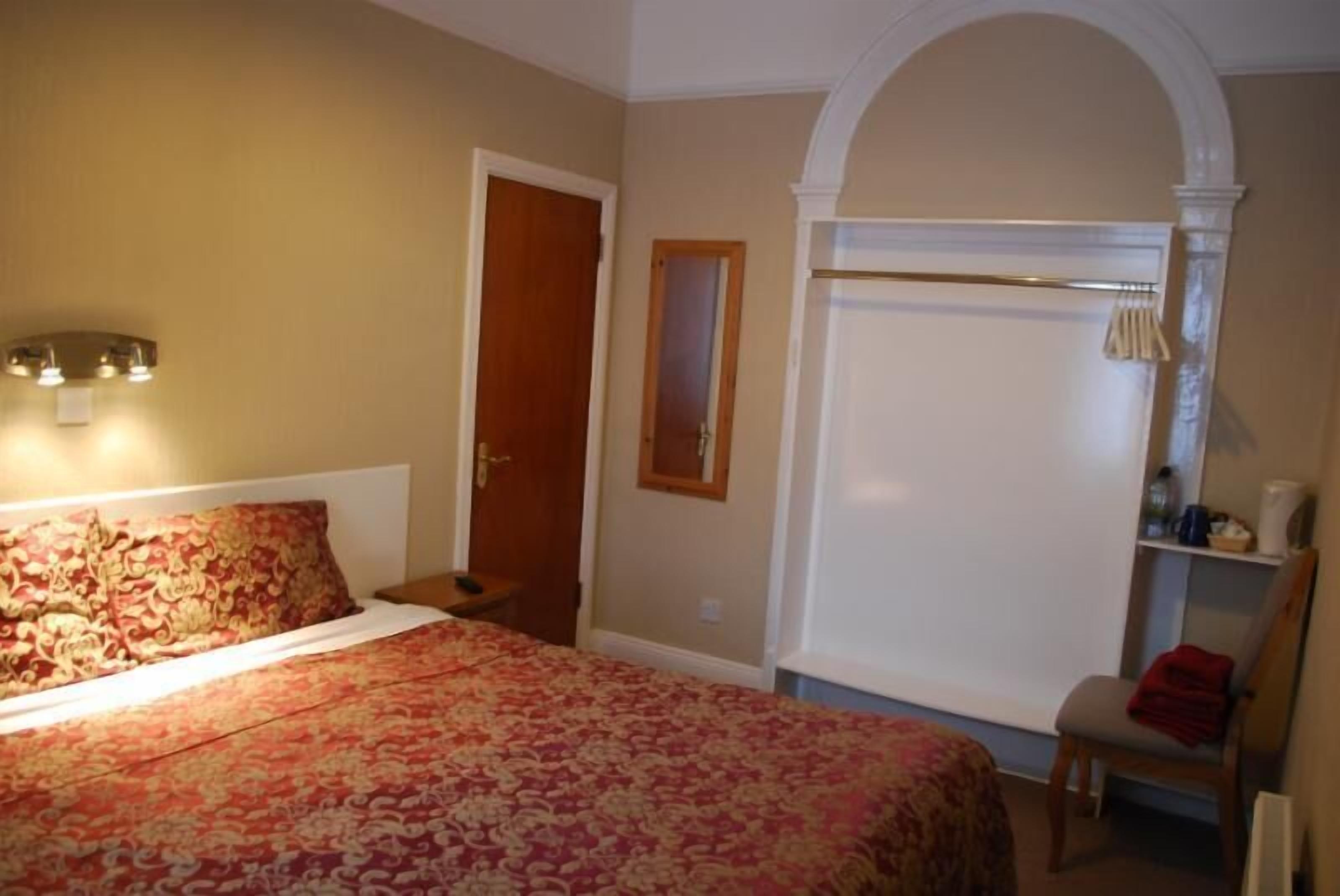 A bedroom with a bed, a nightstand, a chair, a wardrobe, and a mirror.