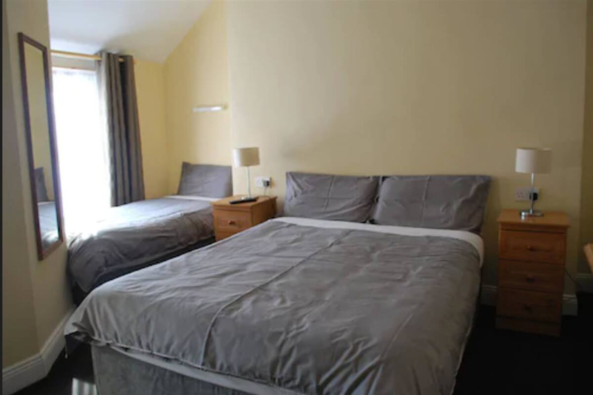 Ein Hotelzimmer mit zwei Einzelbetten, einem Nachttisch aus Holz mit Lampe und einem Spiegel an der Wand.