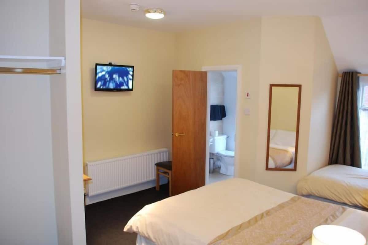 Ein Hotelzimmer mit Bett, Fernseher, Spiegel und einem durchgehenden Türrahmen erkennbaren Badezimmer.