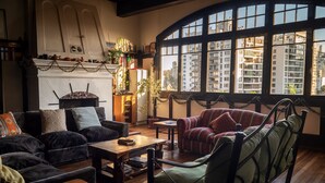 Een gezellige woonkamer met een open haard, een groot raam met uitzicht op gebouwen, en een groene fauteuil.