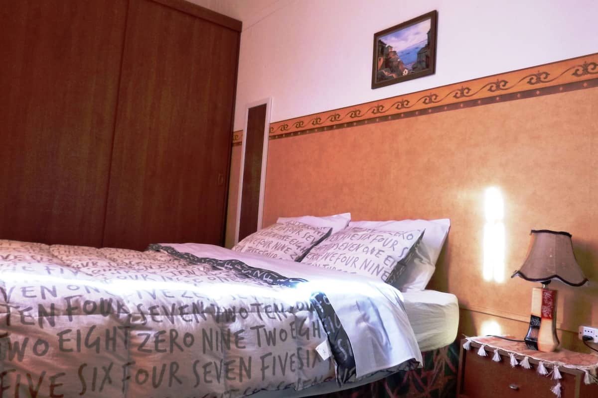 A bedroom with a bed, pillows, a nightstand, a lamp, and a wall-mounted picture.