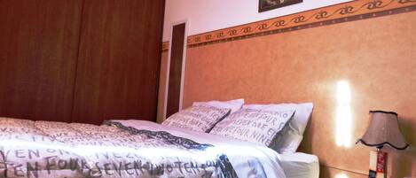 A bedroom with a bed, pillows, a nightstand, a lamp, and a wall-mounted picture.