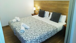 Un letto rifatto con cura, coperta a motivi decorativi, due cuscini e asciugamani arrotolati su un lato.